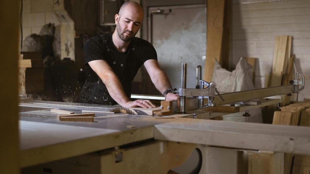 A man cutting wood with a table saw in a workshop.