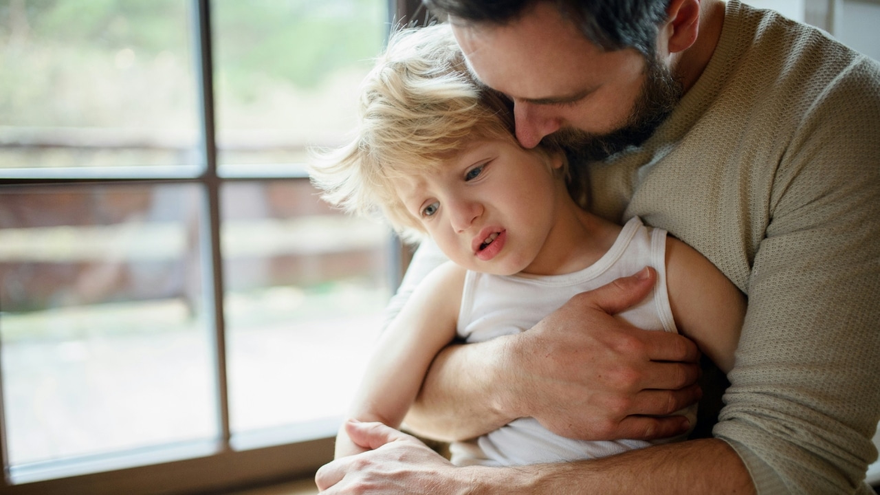 A bearded man holds a young, blonde child closely while looking down at the child.