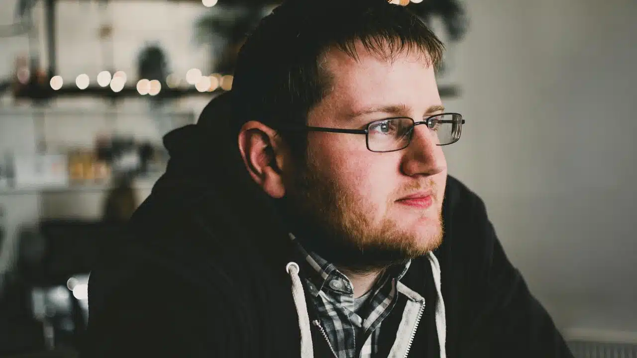 A man wearing glasses and a hoodie sitting indoors