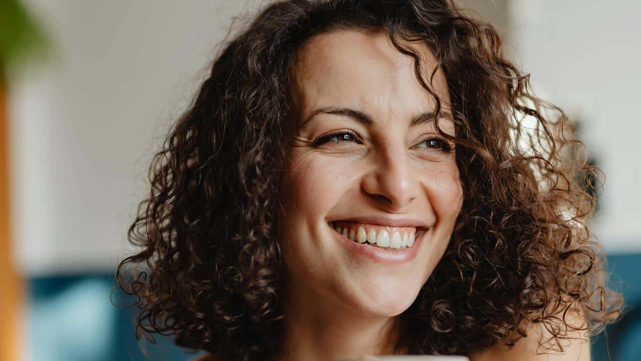 A close-up of a smiling woman with curly hair indoors.