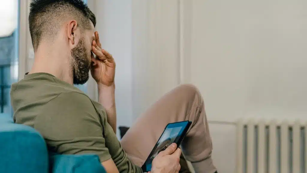 A man holding a tablet and rubbing his forehead, appearing tired or stressed.