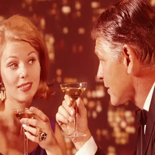 A romantic couple drinking champagne with a city skyline at night in the background.