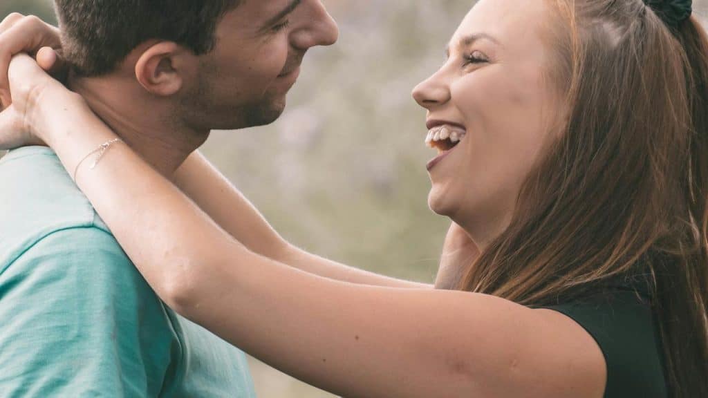 A man and woman embracing each other and smiling outdoors.
