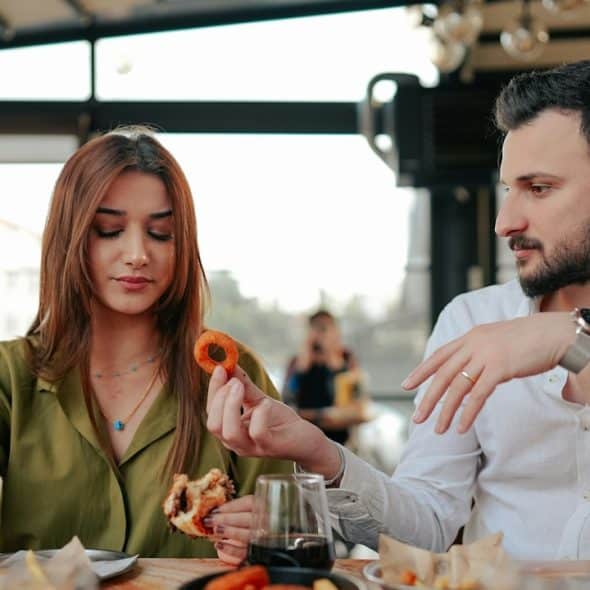 A man offering a pretzel to a woman who looks irritated while declining it.