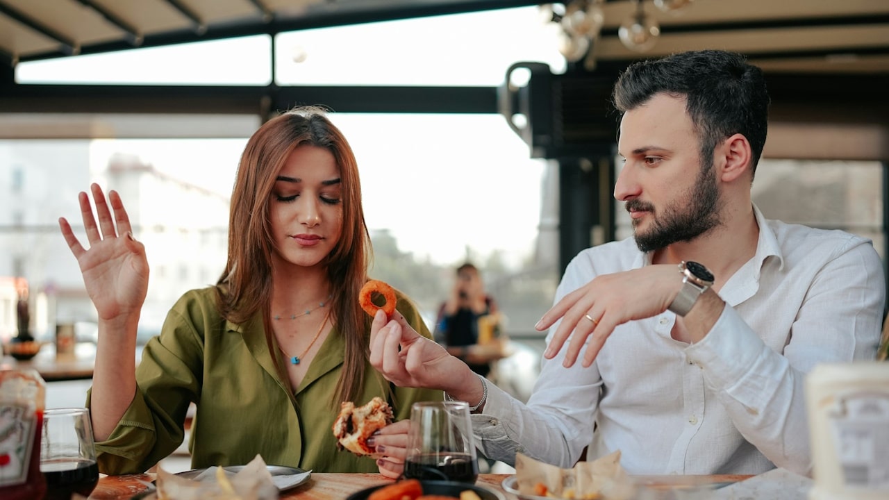 A man offering a pretzel to a woman who looks irritated while declining it.