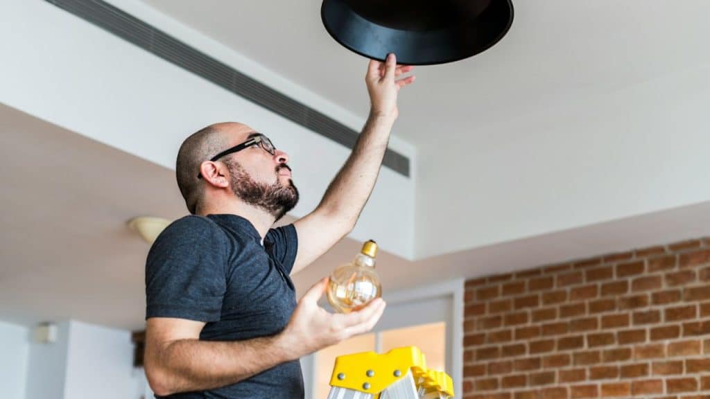 A man in a grey shirt installs a lightbulb.