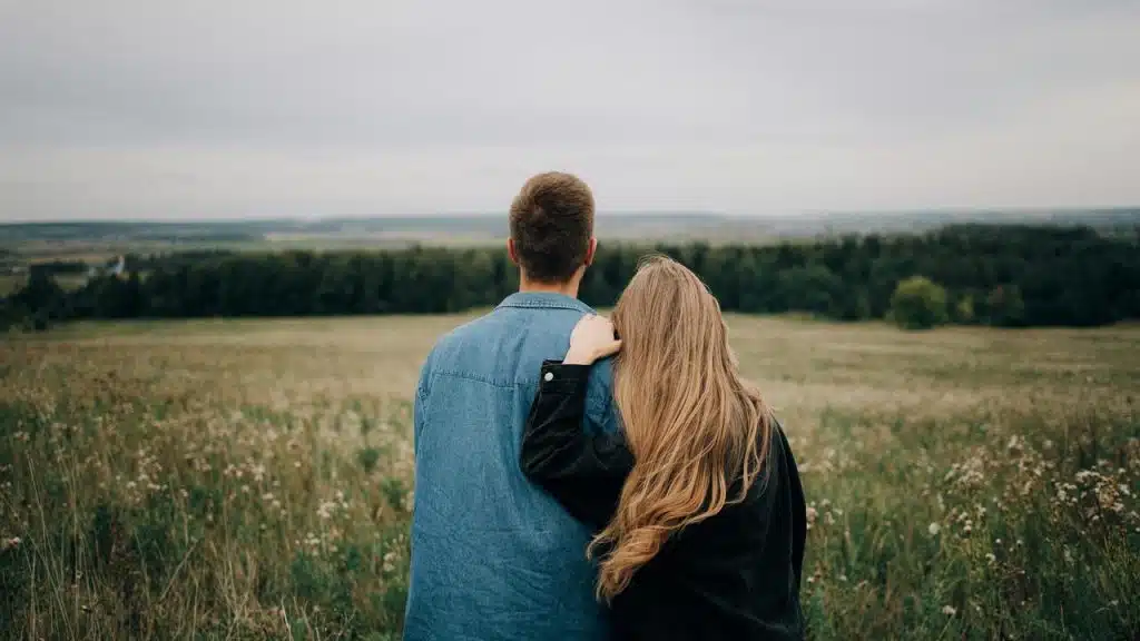 A couple standing in a field with their backs to the camera, looking at the landscape.