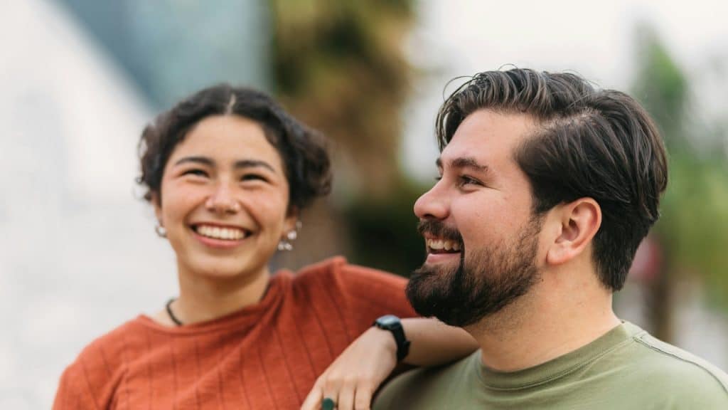 A smiling couple with the woman having her arm placed on the man’s shoulder.