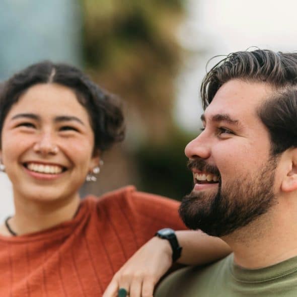A smiling couple with the woman having her arm placed on the man’s shoulder.