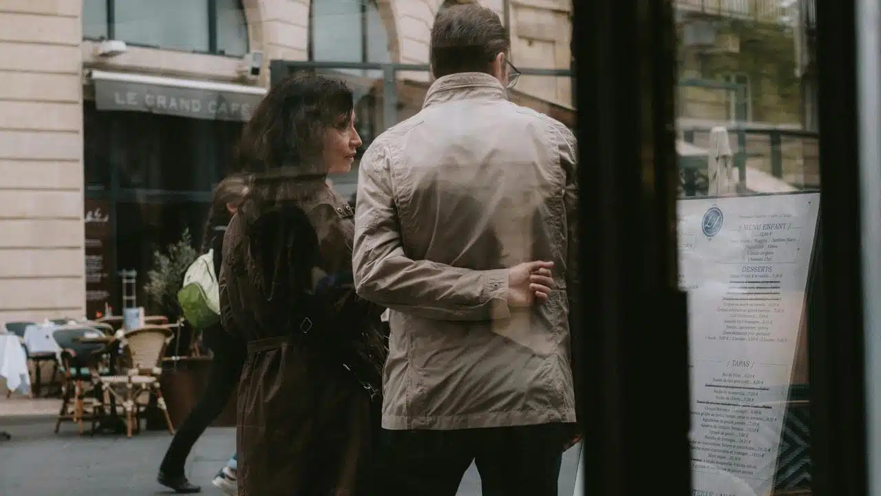 A couple standing close together outside a café, seen through a window.