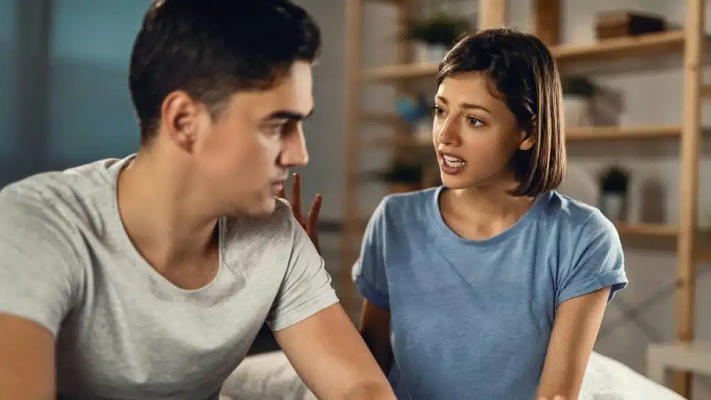 A woman with short hair speaks while a man in a grey shirt looks away.