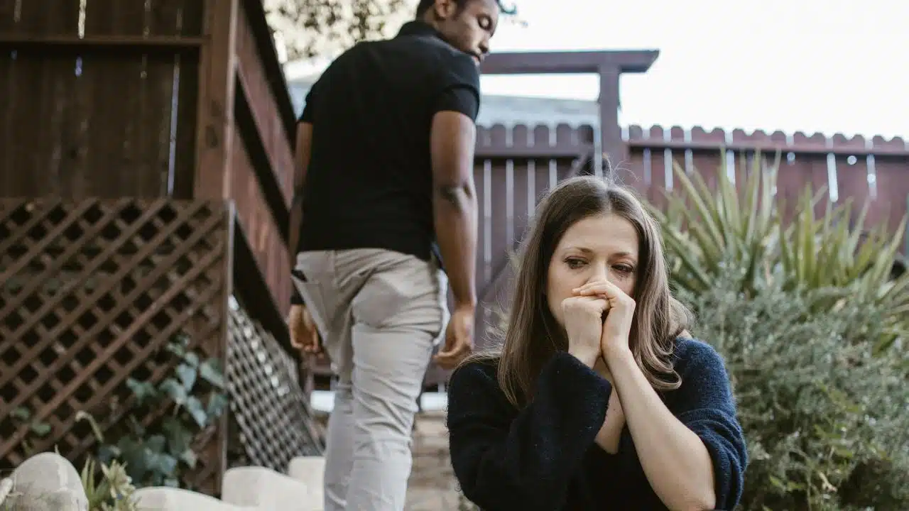 A distressed woman sitting outdoors while a man walks away in the background.