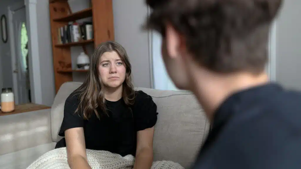 A sad woman looks at a man as they sit together on a couch.