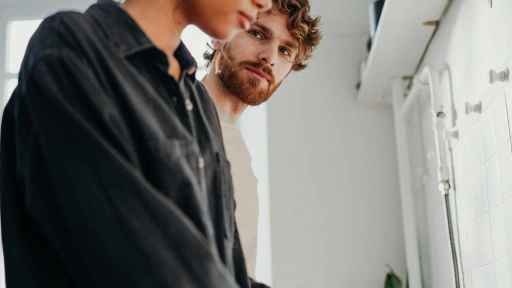 A man looking at another person while standing together in a bright kitchen.