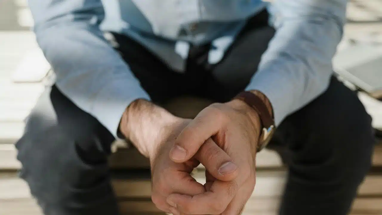 A close-up of a man sitting with his hands clasped together.