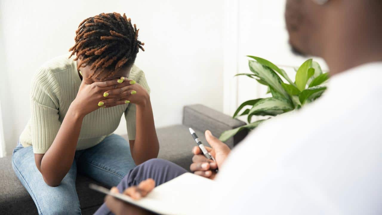 A distressed person sitting with their head in their hands while speaking to someone