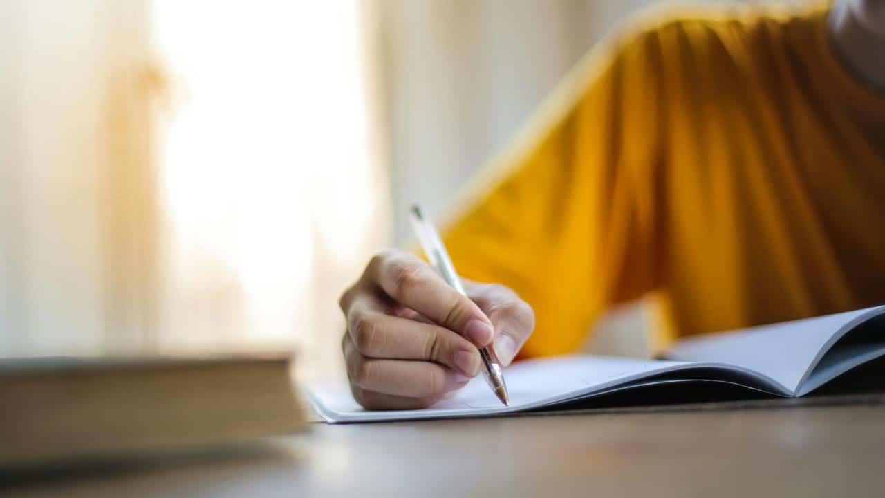 A person writing in a notebook with a pen at a desk.