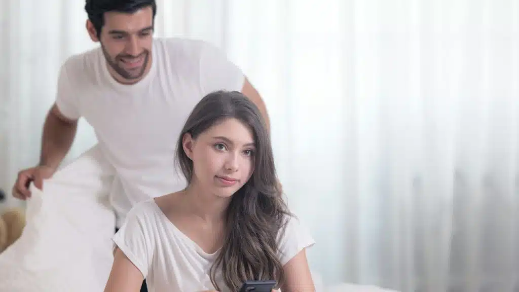 A man looking at his wife using a phone while standing behind her.