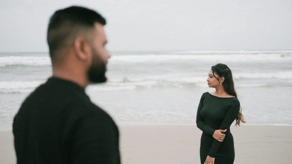 A couple on the beach are facing the ocean.