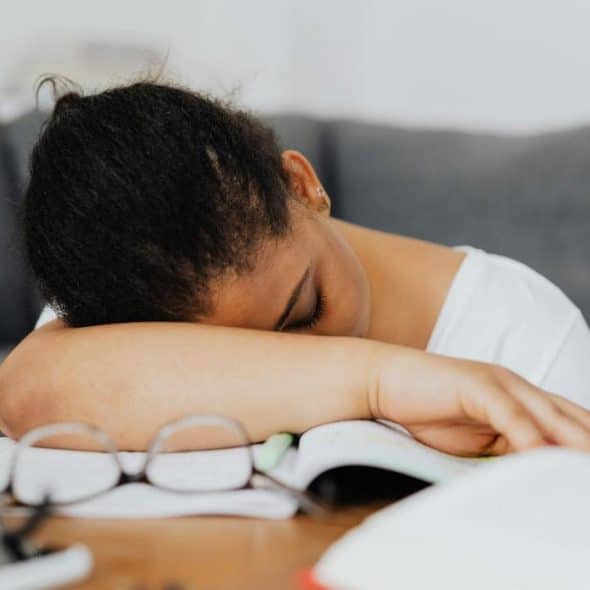 A tired student resting her head on a book at a desk.