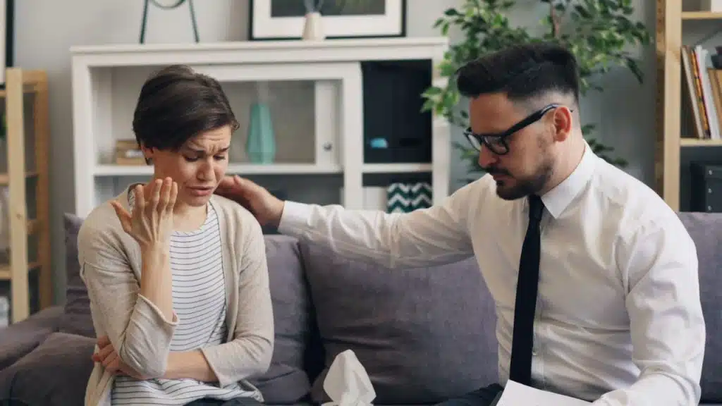 A man in a tie comforts a crying woman by placing a hand on her shoulder.