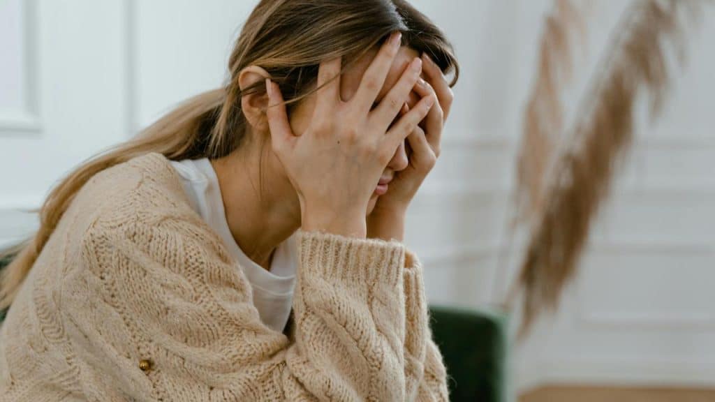 A woman sitting indoors with her face buried in her hands.