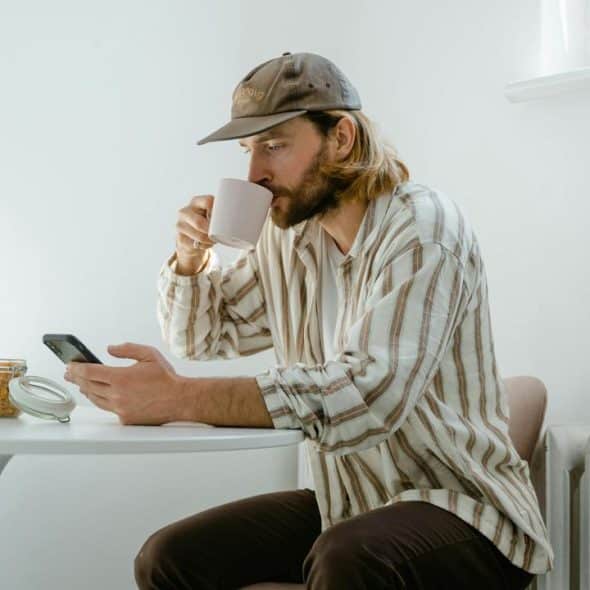 A man drinking coffee while looking at his phone at a table.