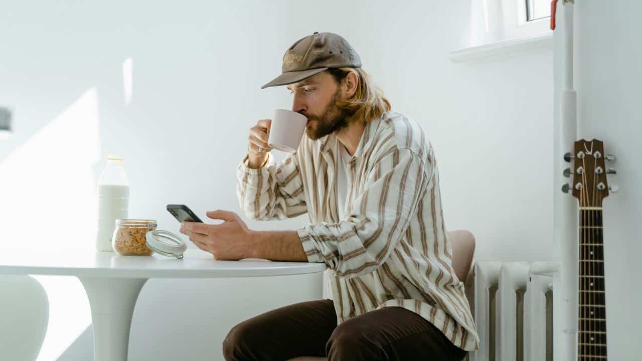 A man drinking coffee while looking at his phone at a table.