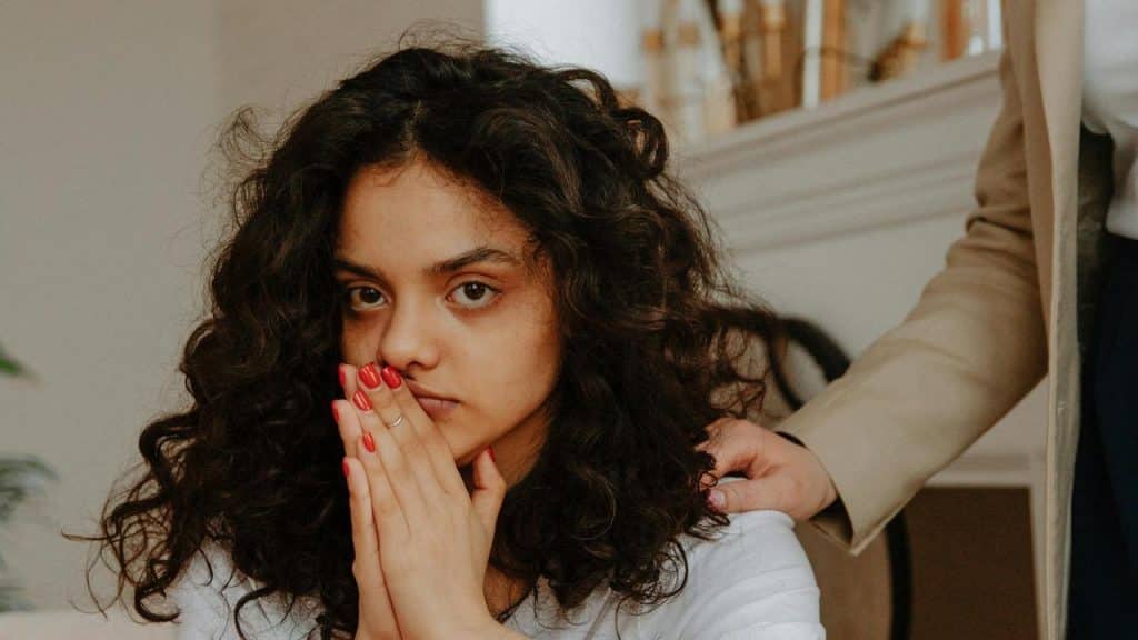 A worried young woman covering her mouth while a hand rests on her shoulder.