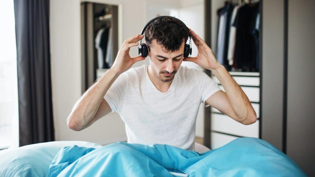 A man listening to a song while sitting on the bed.