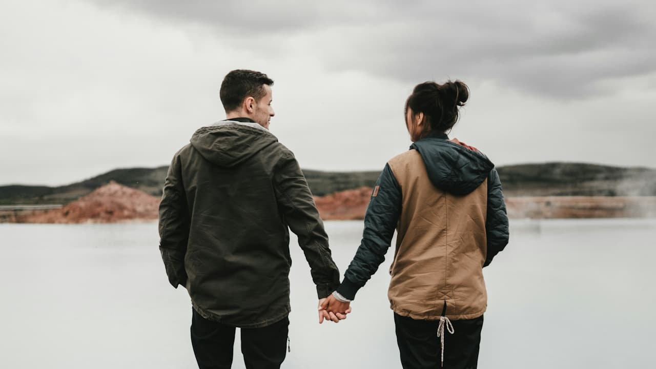 A couple holding hands in front of a lake.