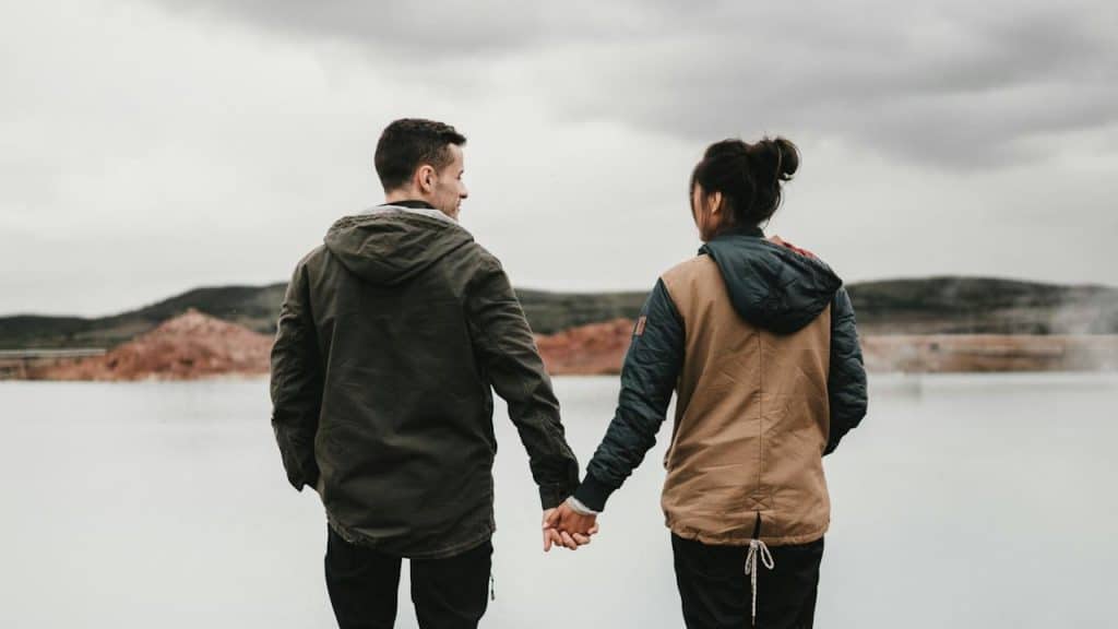 A couple holding hands in front of a lake.