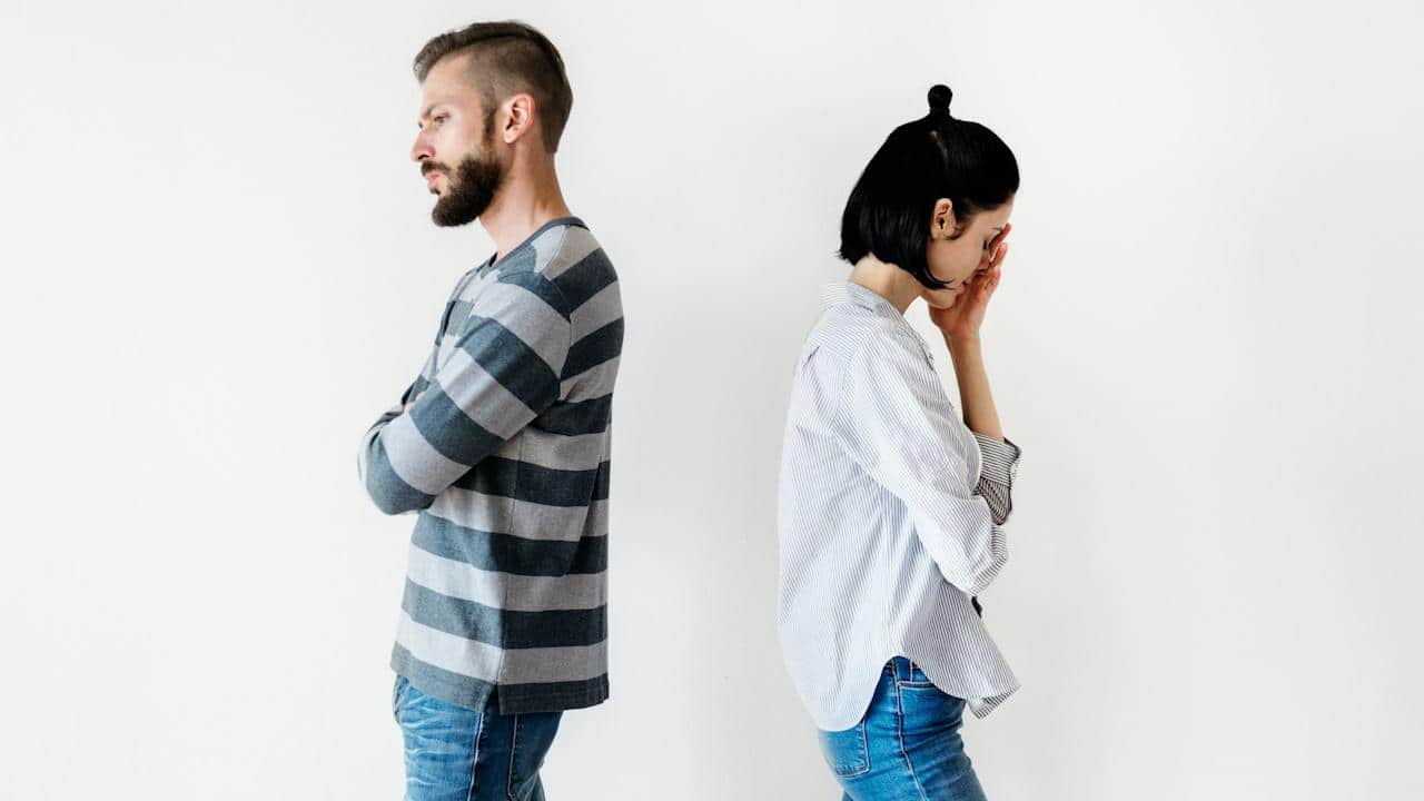 An upset couple standing with their backs against each other.