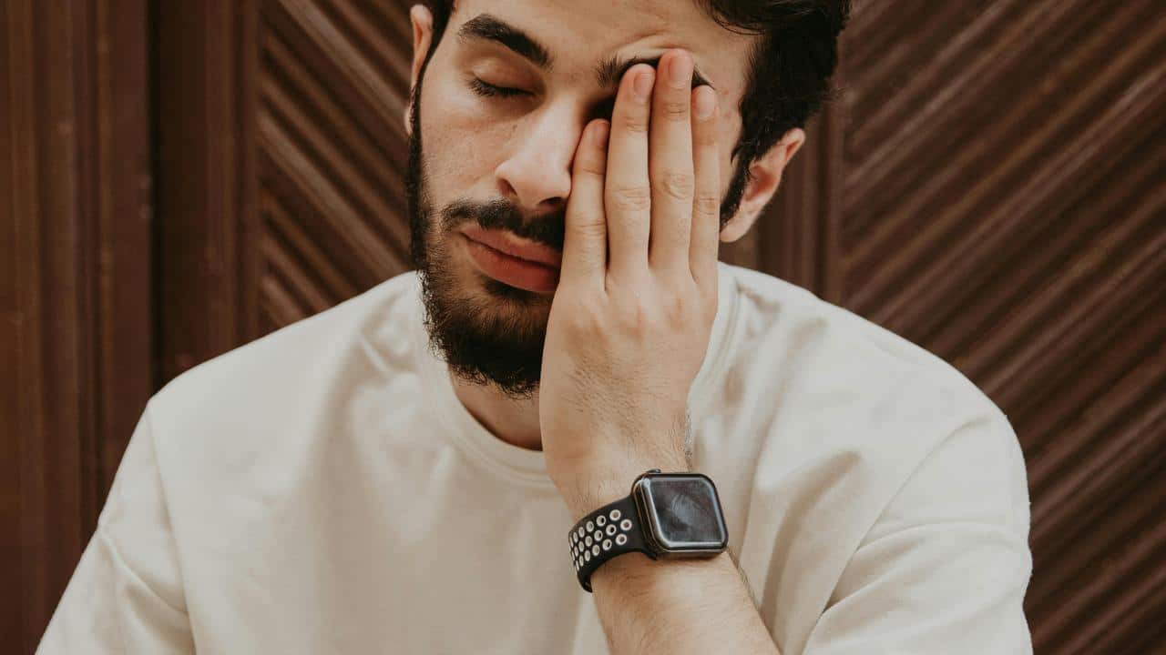 A tired bearded man covering one eye with his hand