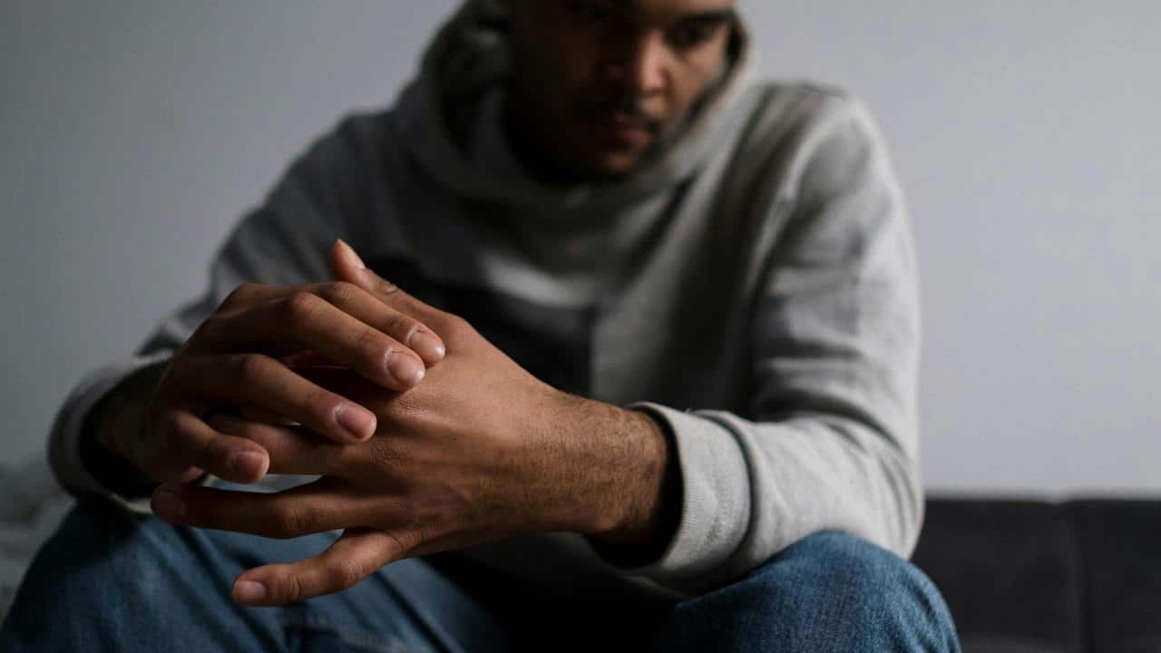 A man sitting with his hands closed together and looking down.