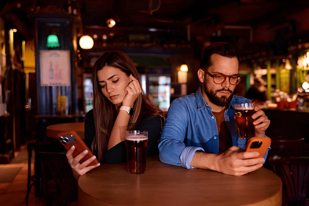Couple at a bar table, holding smartphones and avoiding eye contact