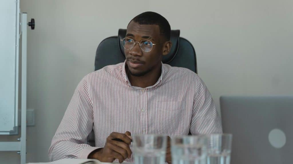 A man wearing glasses sitting at a desk and looking to the side.