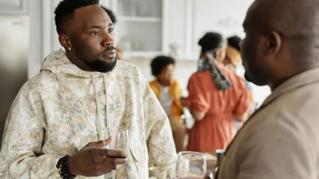 A man holding a drink while talking to another person at a social gathering.
