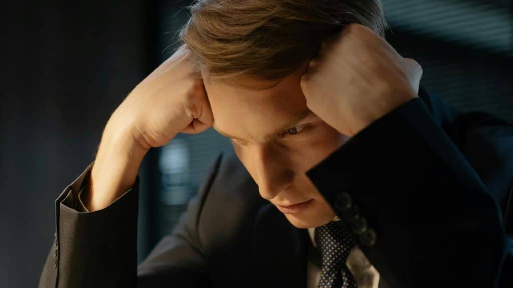 A man in a suit holding his head, looking stressed and deep in thought.