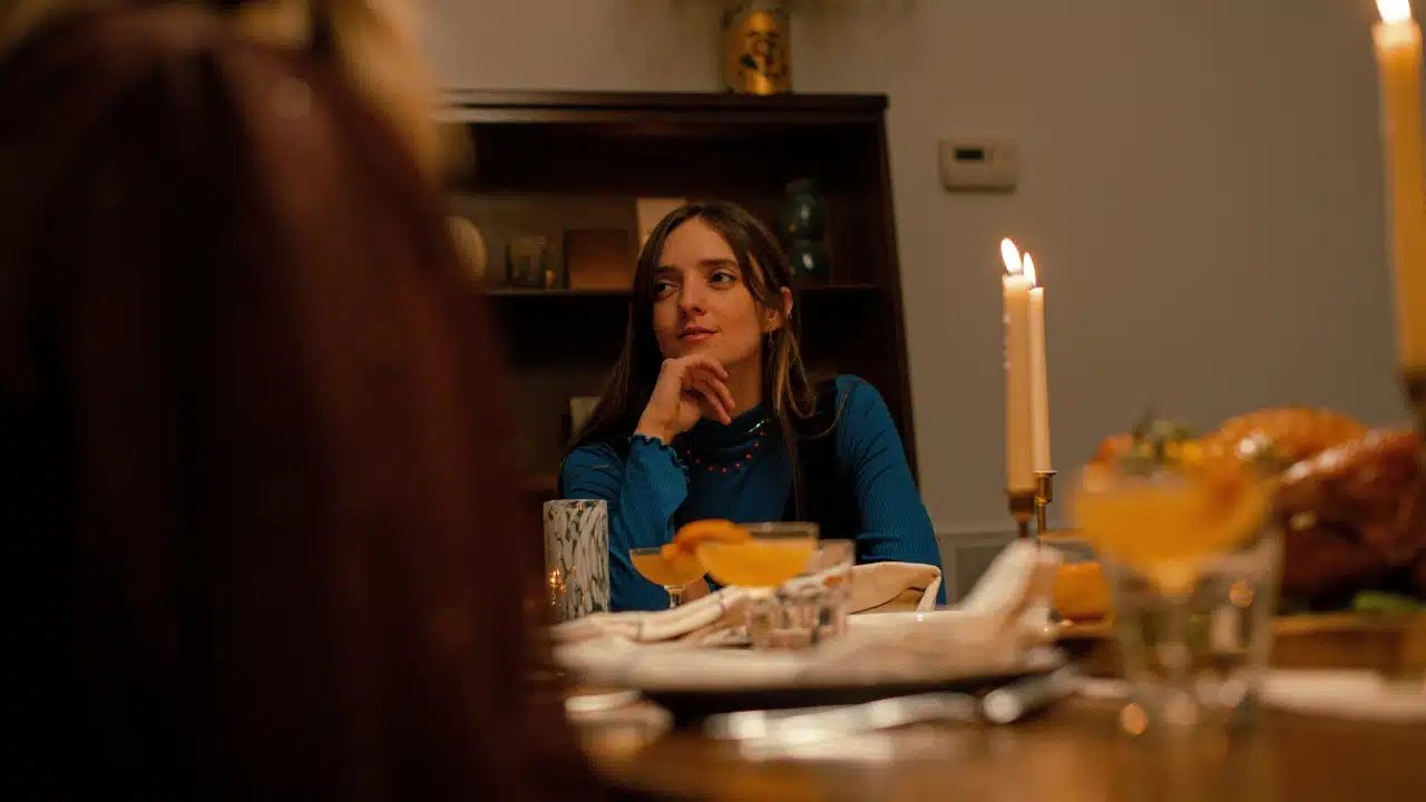A woman in a blue shirt sits at a candlelit dinner table, resting her chin on her hand.