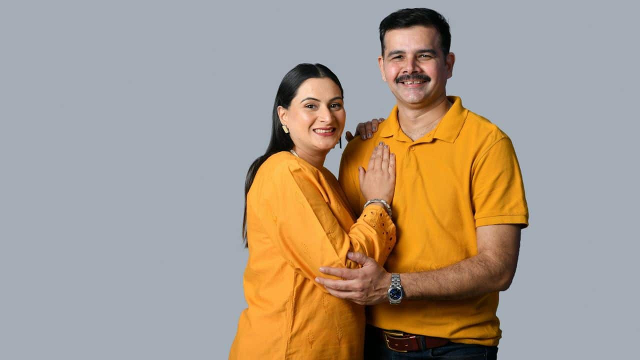 A man and woman in yellow shirts smile together against a plain grey background.