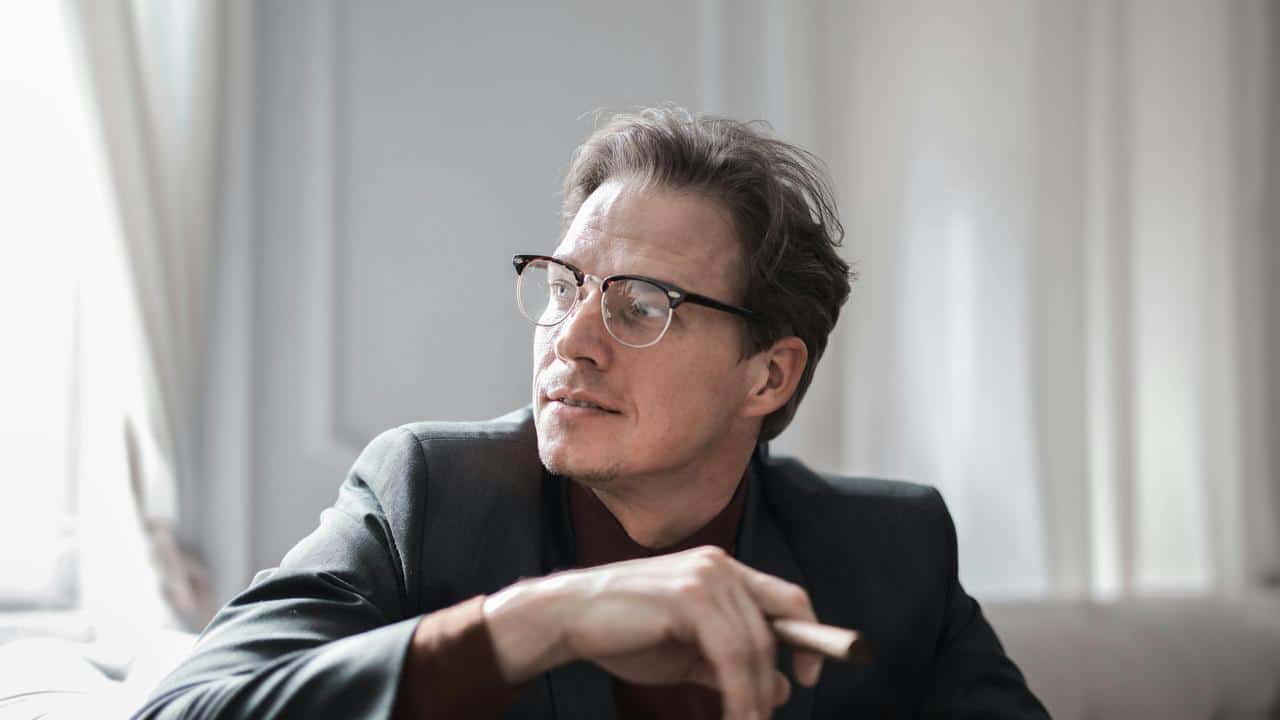 A man wearing glasses looking off to the side while sitting indoors.