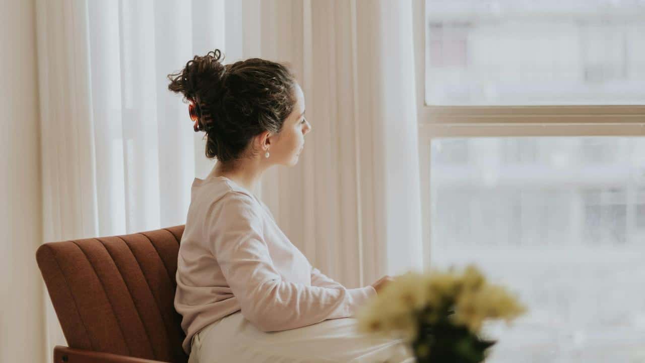 A person sitting on a chair and gazing out of a window thoughtfully.