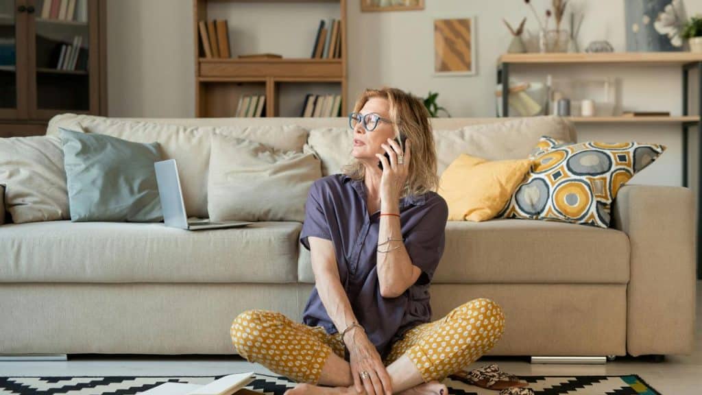 A woman sitting on the floor at home talking on the phone.