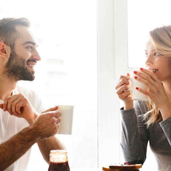 An amazing, young, loving couple sitting at the kitchen table having breakfast and talking with each other.