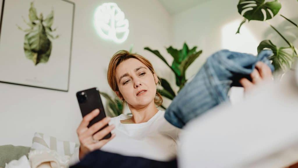 A woman holding a smartphone while examining a piece of clothing.