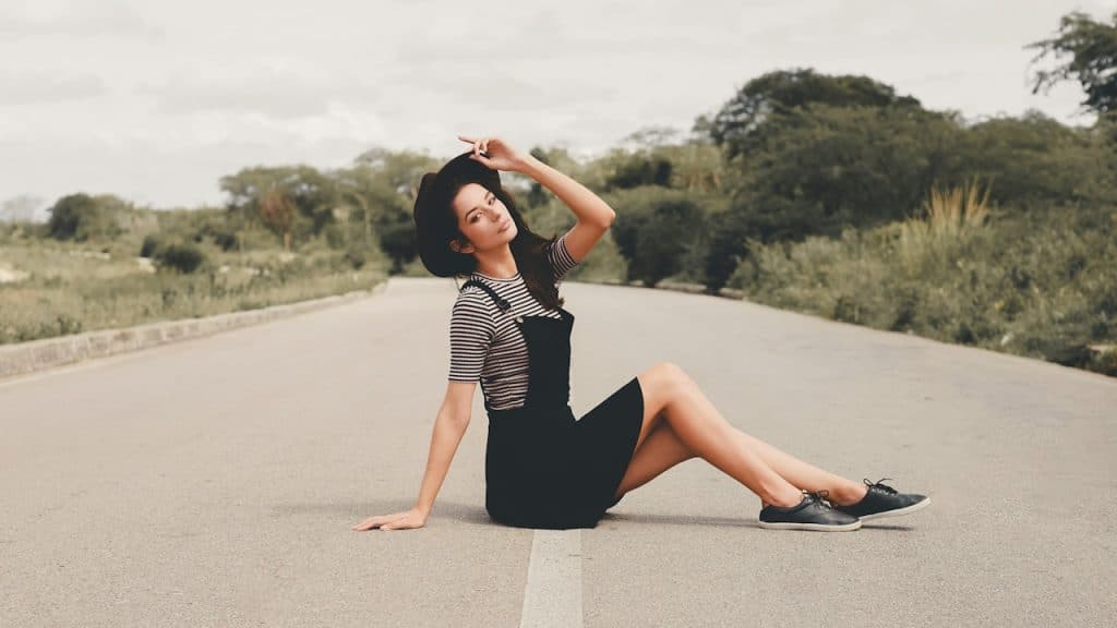 Woman in black-and-white dress standing on gray asphalt road during daytime.