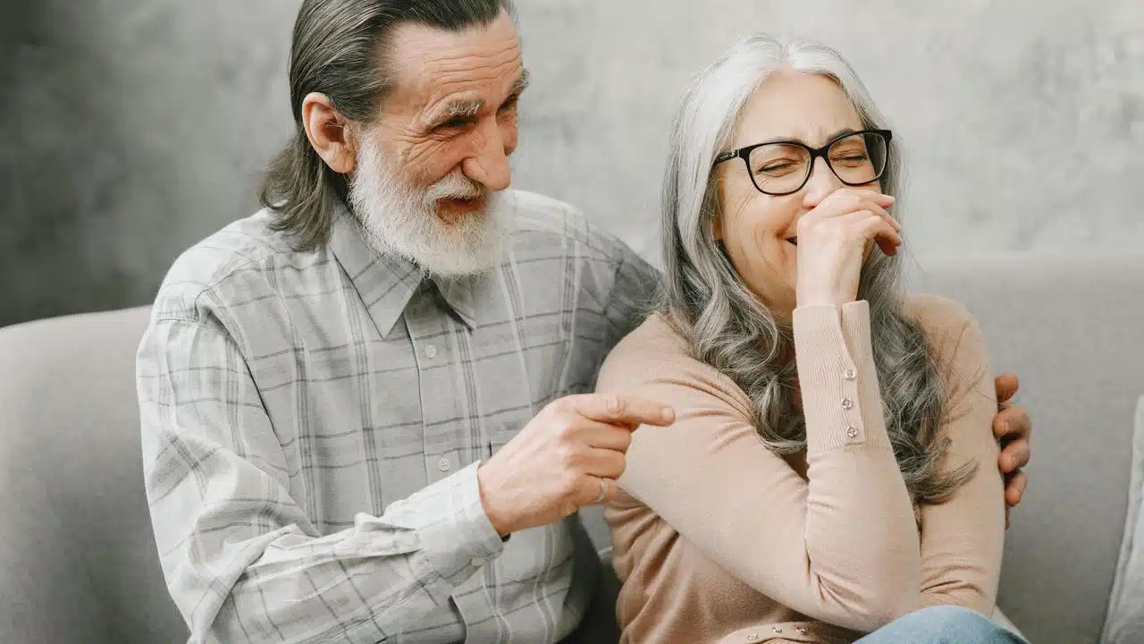 A senior couple sitting on a couch, laughing together.