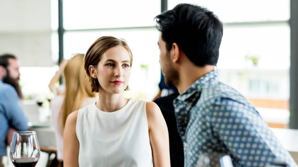 A woman in a white top looks at a man in a blue shirt.