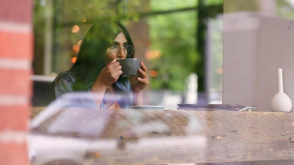 A woman with glasses sipping coffee at a cozy café by a window.